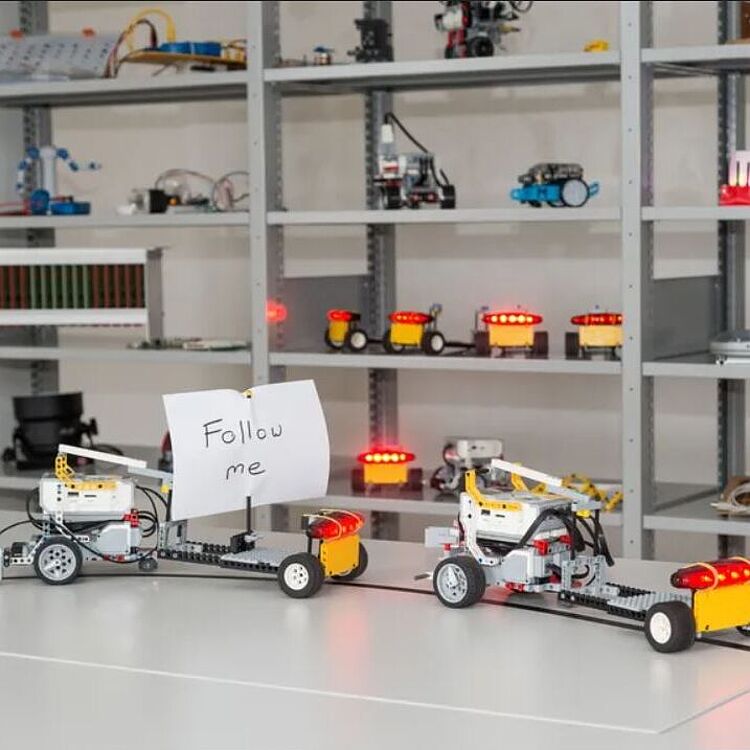 Selbsterstellte kleine elektronischen Fahrzeuge aus Lego-Technik, dahinter ein Regal mit weiteren kleinen Fahrzeugen