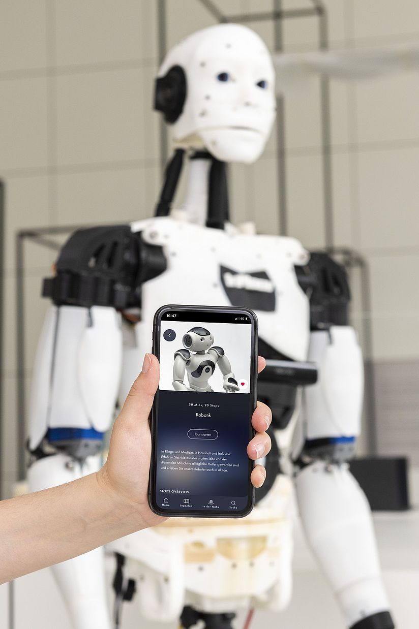 Mit der Deutschen Museum App Ausstellungen entdecken Hand hält ein Smartphone mit der Deutsches Museum App vor ein Exponat in der Ausstellung Robotik