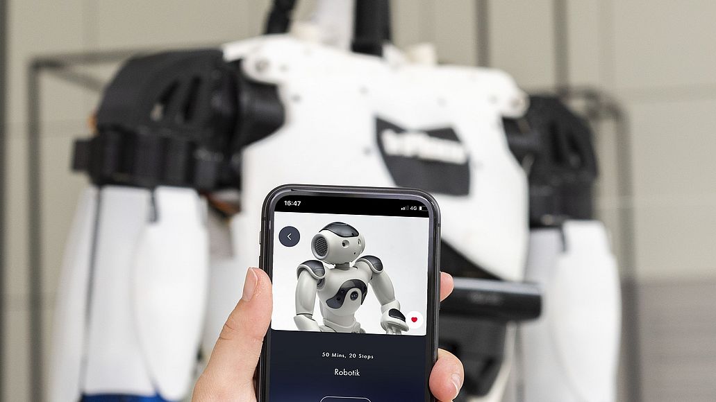 Mit der Deutschen Museum App Ausstellungen entdecken Hand hält ein Smartphone mit der Deutsches Museum App vor ein Exponat in der Ausstellung Robotik