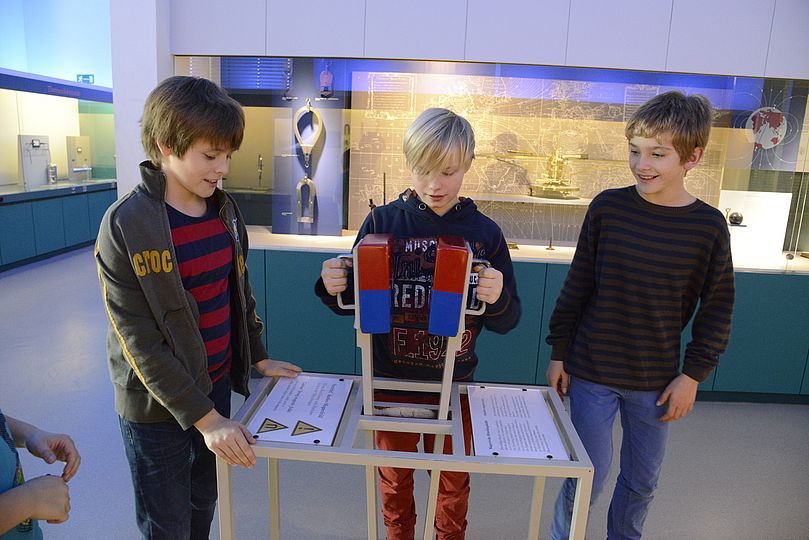 Drei Kinder an einer Demonstration mit einem großen Magneten in der Physik-Ausstellung.