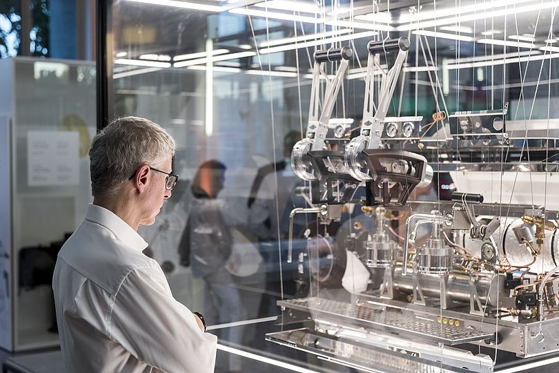 Besucher betrachtet Kaffeemaschine in einerr Vitrine.