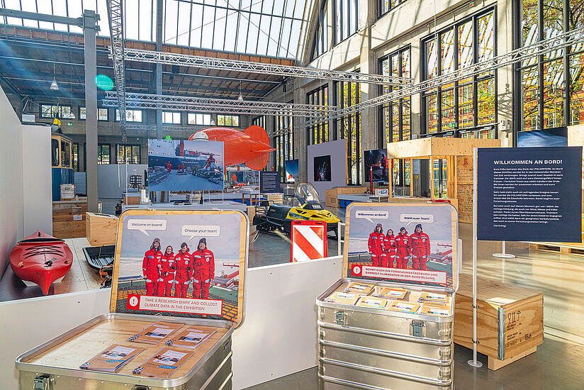 Im Vordergrund stehen zwei offene Metallkisten mit der Aufschrift: 