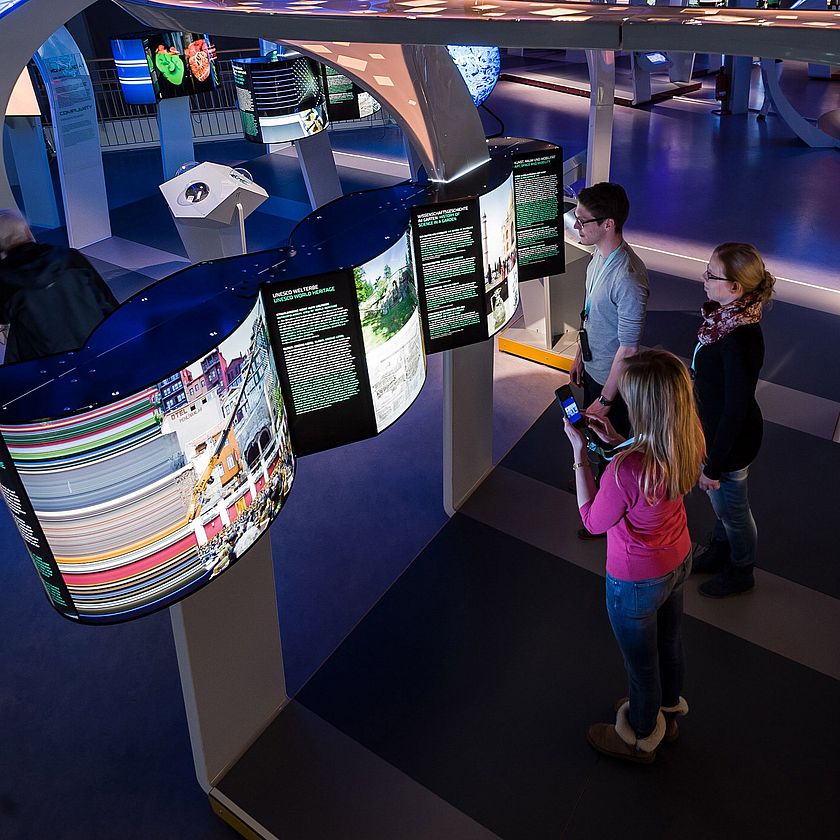 EIne Ausstellung mit bunten Leuchtkästen und darin drei Besucher.