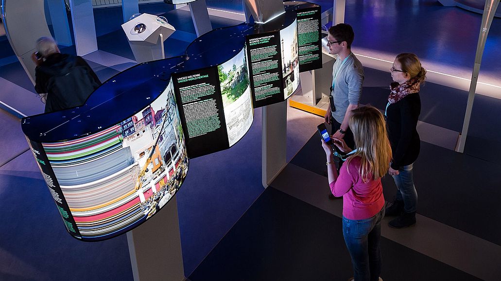 EIne Ausstellung mit bunten Leuchtkästen und darin drei Besucher.