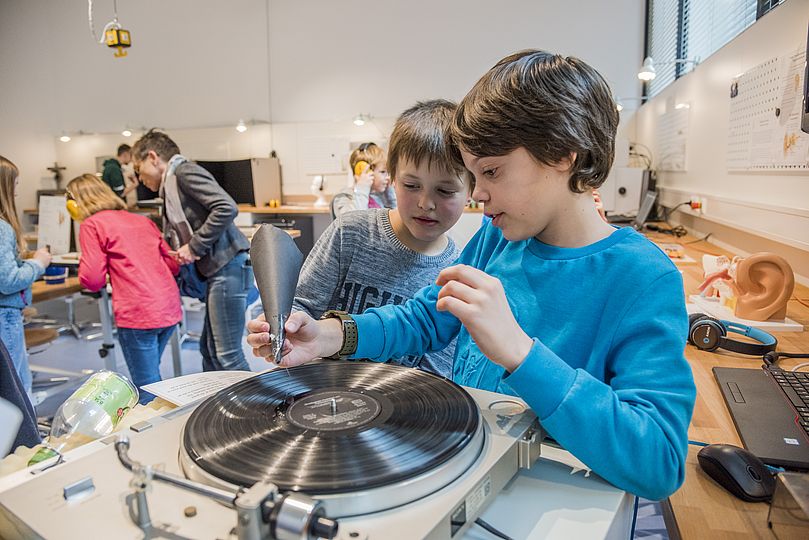 Zwei Schüler experimentieren. Sie versuchen mit Hilfe eines Trichters aus Pappe und einer dort befestigten Nadel, Musik von einer Schallplatte hören zu können.