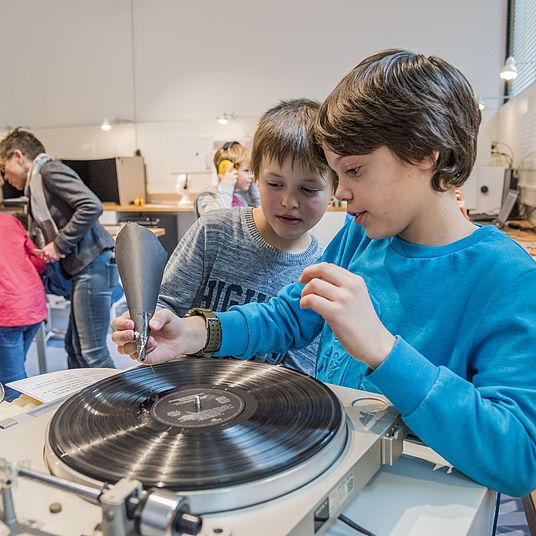Hör-Werkstatt Zwei Schüler experimentieren. Sie versuchen mit Hilfe eines Trichters aus Pappe und einer dort befestigten Nadel, Musik von einer Schallplatte hören zu können.