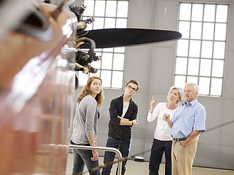 Vier Personen stehen in der Ausstellung und nehmen an einer Führung teil.