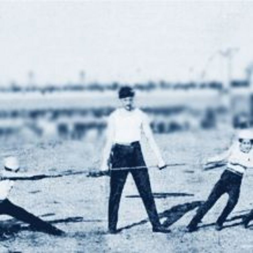 Kinder ziehen Seil. Links ziehen 4 Kinder, am rechten Ende 5 Kinder. In der Mitte steht ein Mann. Er hält das Seil mit seiner linken Hand fest.
