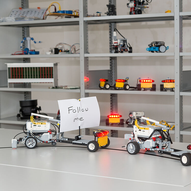 LKW Kolonne aus drei EV3 Robotern. Am ersten LKW ist ein Papierschild mit "Folgt mir" angebracht.