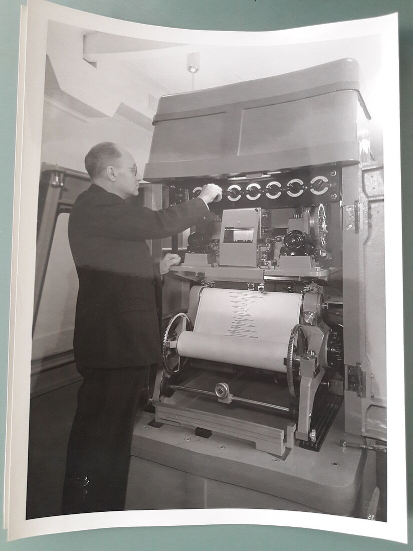 Rauschelbach steht an der Druckerseite des Rechners und stellt etwas an der Technik ein.