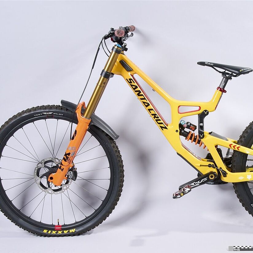 Mountainbike von der Seite fotografiert. Besonderheiten: gelber Rahmen, hohe Federung, große Reifen. Es ist deutlich, dass es sich um ein stabiles und optimiertes Sportgerät handelt.