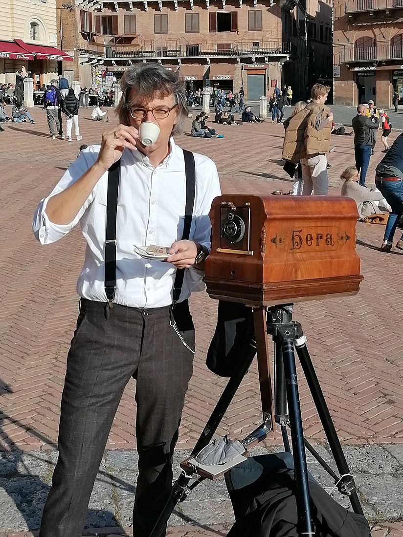 Sebastian Schlagenhaufer steht neben seiner Camera Minutera, einem Holzkasten auf einem Tripod und trinkt einen Espresso.