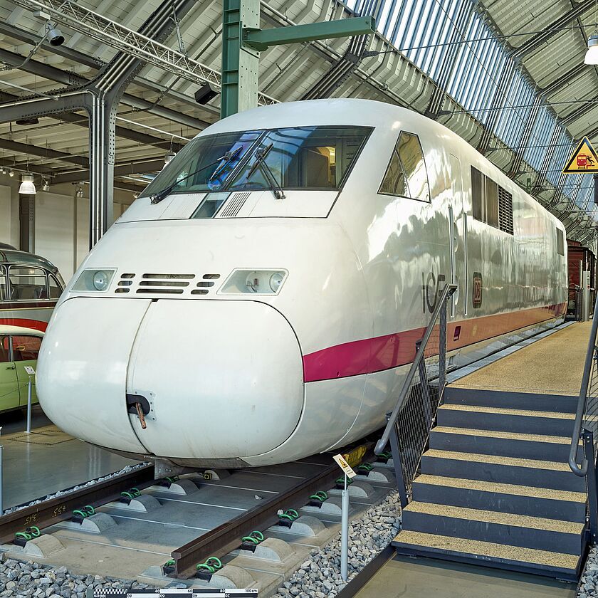 Triebkopf eines weißen InterCityExperimental mit rotem Zierstreifen, ausgestellt im Verkehrszentrum auf kurzen Schienenstücken mit Zugangstreppe.