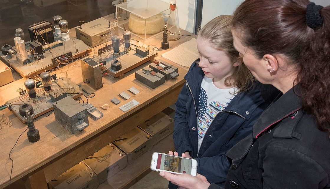 Mutter mit Tochter mit offener Deutsches Museum App vor dem Kernspaltungstisch.