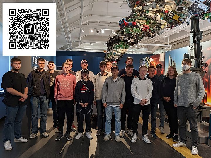 Eine Schulklasse vor dem Schrotttornado in der Ausstellung Elektronik. Links oben, in der Ecke, befindet sich der QR-Code zum Actionbound "Erkundet Recycling mit Actionbound".