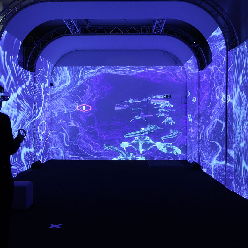 Raumprojektion VRlab Foto einer Raumprojektion in blau mit einer Person mit VR Brille auf dem Kopf im Vordergrund