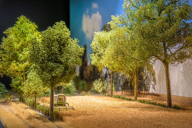 Diorama zeigt einen Traktor auf einem Feld mit angrenzenden Bäumen.