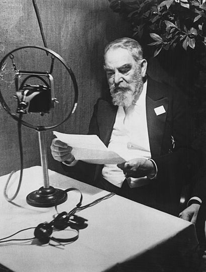 Oskar von Miller liest vor einem Mikrofon sitzend seinen Text für eine Radioansprache durch.