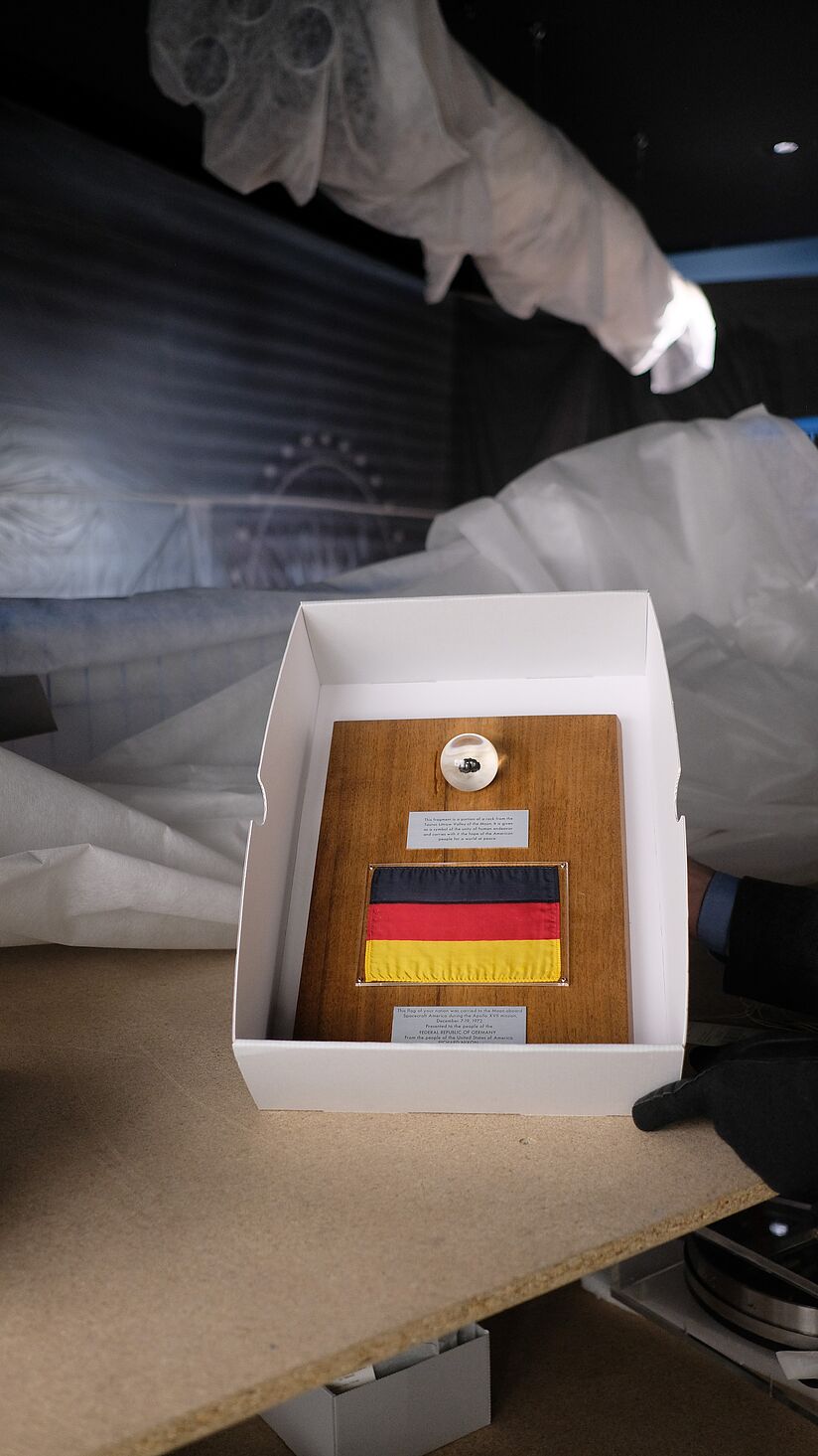 •	Ausstellungsobjekt bestehend aus Mondgestein, Plakette und Deutschlandflagge in einem Karton während des Umbaus