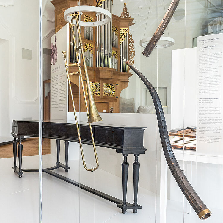 Cembalo, Posaune, Kummer Zink und Tenor Zink in einer Vitrine. Im Hintergrund befindet sich die Orgel von Jürgen Ahrend.