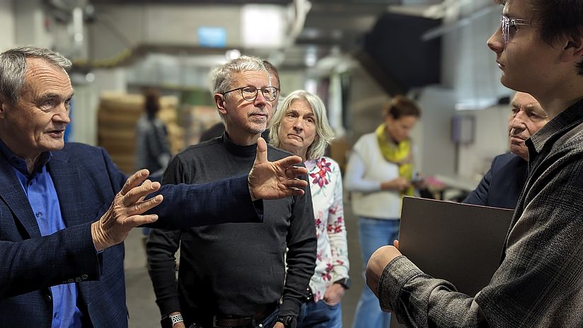 5 Menschen stehen in einem Fabrikraum und erhalten eine Führung.