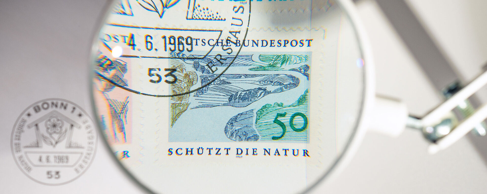 Kleine Lupe vergrößert eine der vier Briefmarken und einen Teil des Stempels. Die Briefmarke zeigt einen Fluss, der sich durch die Natur schlängelt. Zu lesen ist "Schützt die Natur".