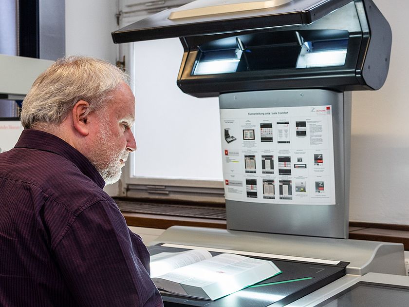 Scannen im Lesesaal der Bibliothek. Ein Benutzer scannt ein Buch am Buchscanner im Lesesaal.