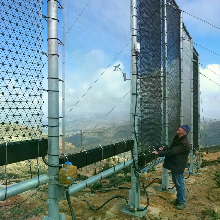 Großes Netz das auf einem Berg im Nebel steht. Eine Person steht vor dem Netz und betrachtet es.
