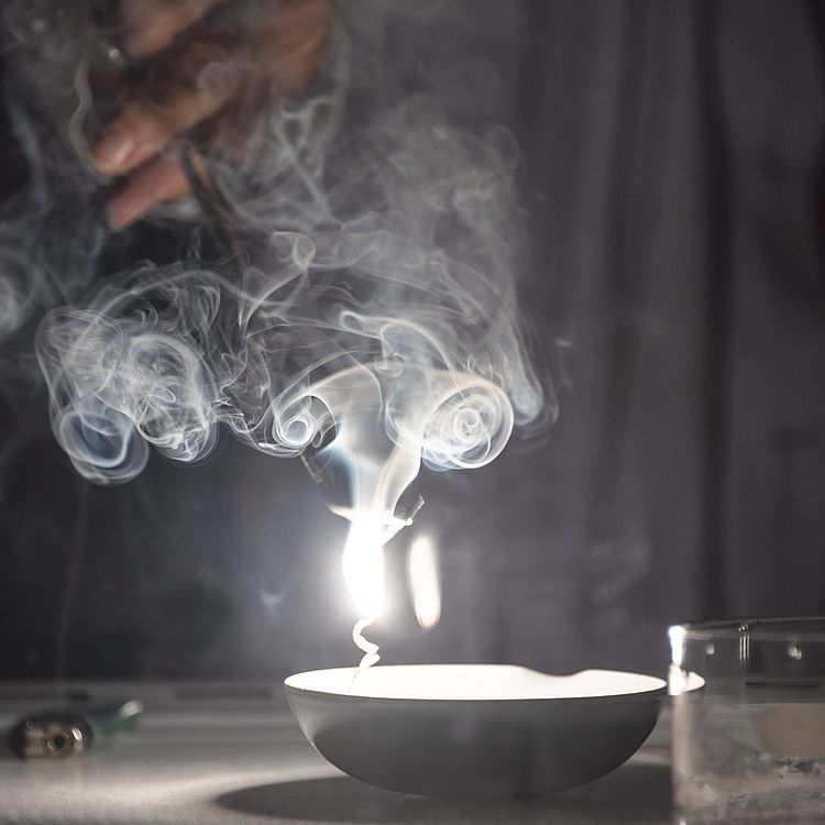 Eine Mitarbeiterin der Ausstellung Chemie zündet im Labor Salze an und eine weiße Flamme und Rauch sticht empor.