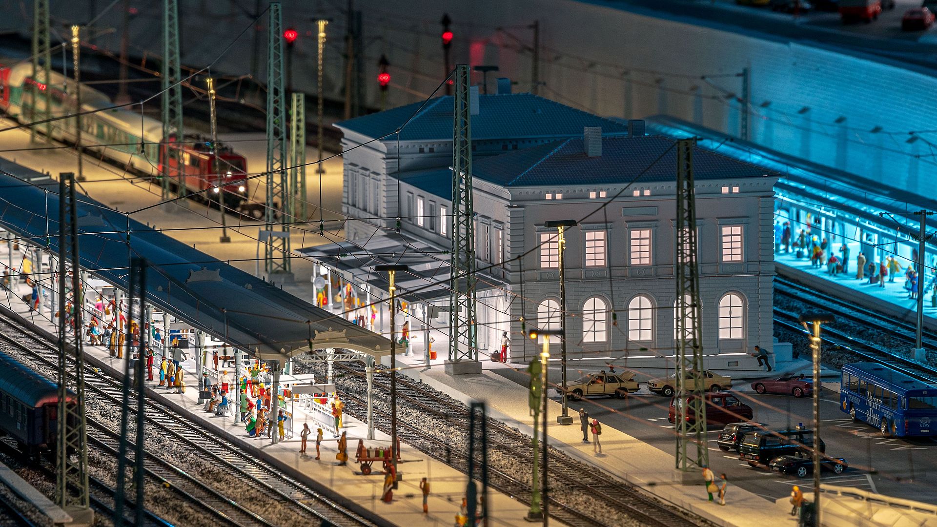 Blick auf die beleuchtete Modellbahnanlage, Gleise, beleuchtetes Bahnhofsgebäude und Lichter der Stellwerke.