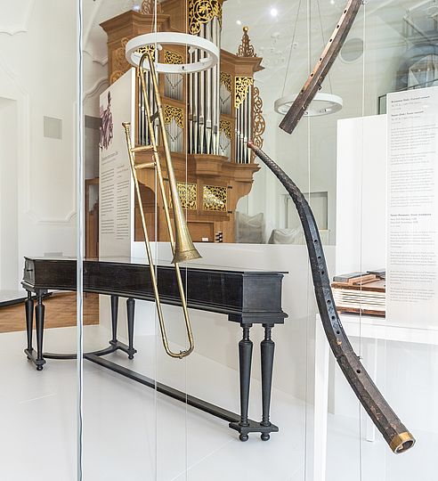 Cembalo, Posaune, Kummer Zink und Tenor Zink in einer Vitrine. Im Hintergrund befindet sich die Orgel von Jürgen Ahrend.