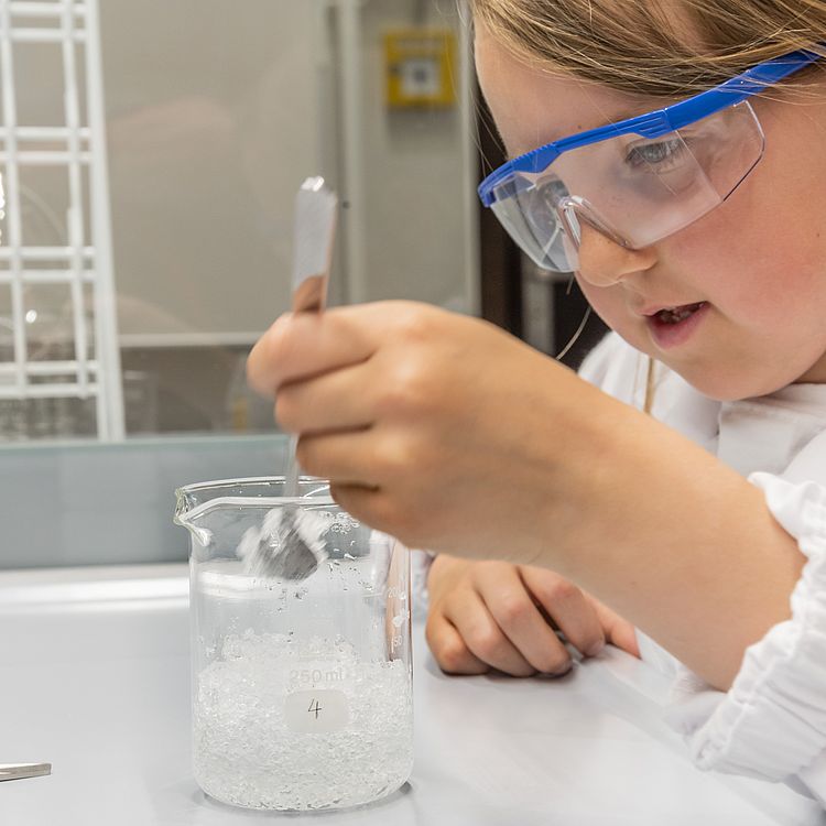 Junges Mädchen mit Schutzbrille experimentiert beim Chemie-Workshop Säuren und Basen.