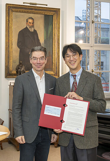 Zwei Männer mit einer Urkunde vor dem gemalten Porträt von Oskar von Miller