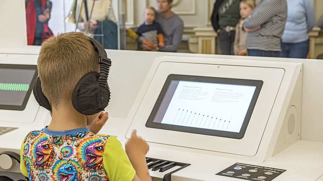 Ein Junge sitzt im Deutschen Museum vor einer Hands-On-Station in der Ausstellung „Musikinstrumente“. Mit den ertastbaren Elementen der Station kann er verschiedene Stimmsysteme untersuchen und die entstehenden Klänge wahrnehmen.
