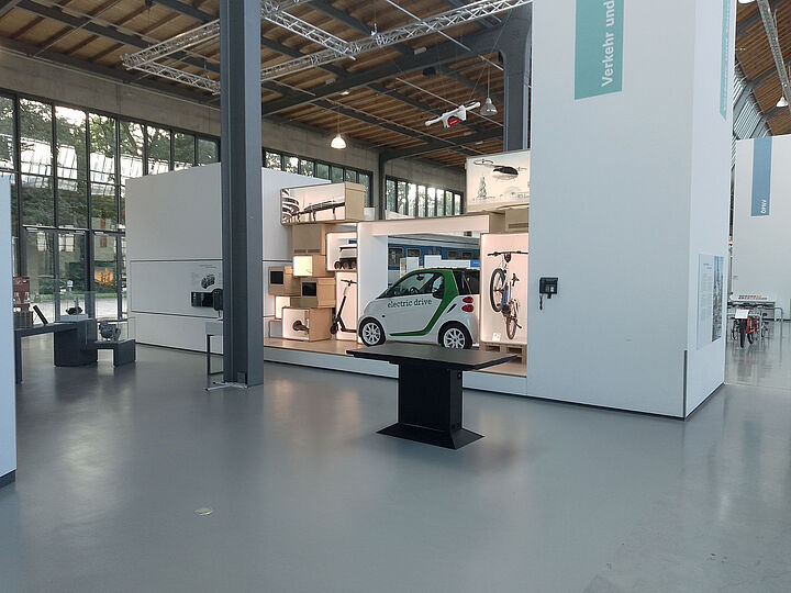 Der Medientisch in Halle I im Verkehrszentrum. Dahinter eine Vitrine mit E-Fahrzeugen.