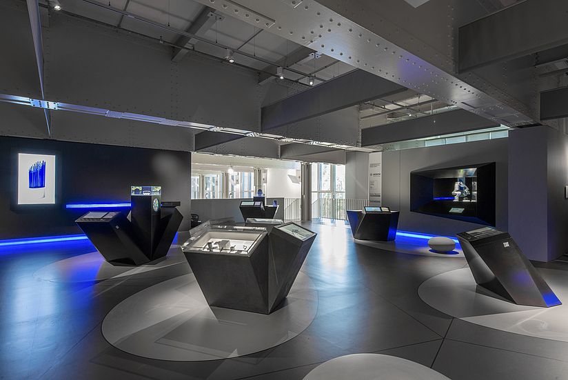 Im abgedunkelten Ausstellungsraum stehen angestrahlte Module zu jedem der zehn ausgestellten Projekte. Gestaltet mit kantigen Kuben.