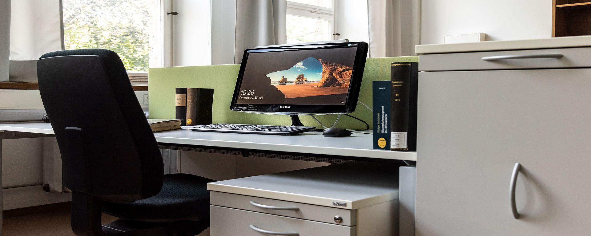 Arbeitsplatz eines Gastwissenschaftlers. Ein PC-Bildschirm und einige Bücher stehen auf dem Tisch.
