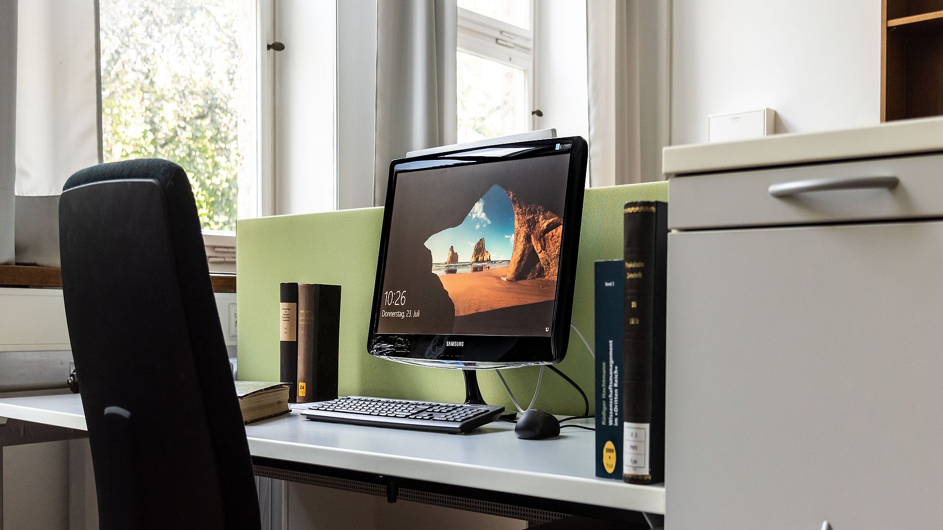 Arbeitsplatz eines Gastwissenschaftlers. Ein PC-Bildschirm und einige Bücher stehen auf dem Tisch.