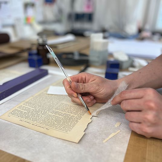 Buchbinderei: Leim wird mit Pinsel auf Papier aufgetragen