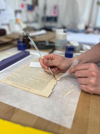 Buchbinderei: Leim wird mit Pinsel auf Papier aufgetragen