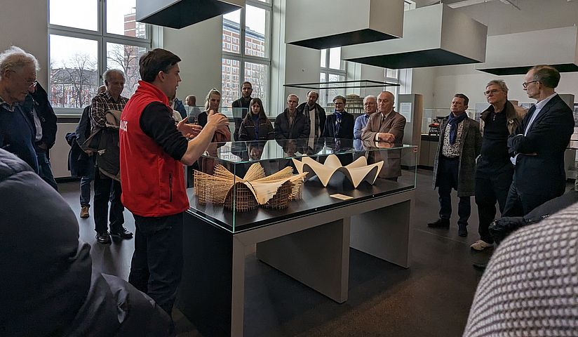 Zahlreiche Personen stehen um ein Exponat und ein Kurator erklärt etwas dazu.