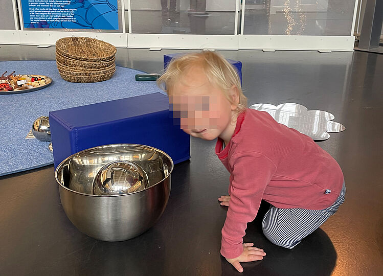 Kleinkind schaut frech in die Kamera und hat Metallschüsseln und bunte Klötze vor sich