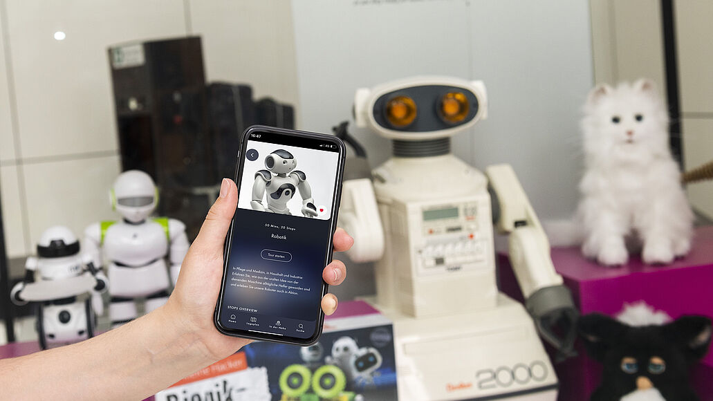 Hand hält Smartphone mit Deutsches Museum App in der Ausstellung Robotik