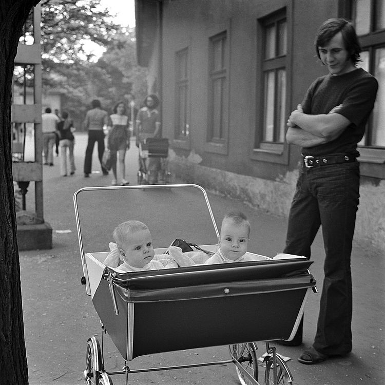 Schwarz-weiß Foto zeigt zwei Kleinkinder in einem Doppelkinderwagen der 70er Jahre.