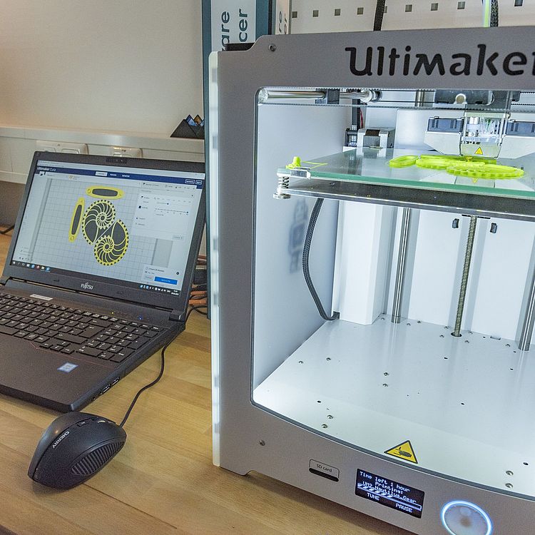 Laptop mit offener Druckgrafik neben einem 3D-Drucker in Aktion.